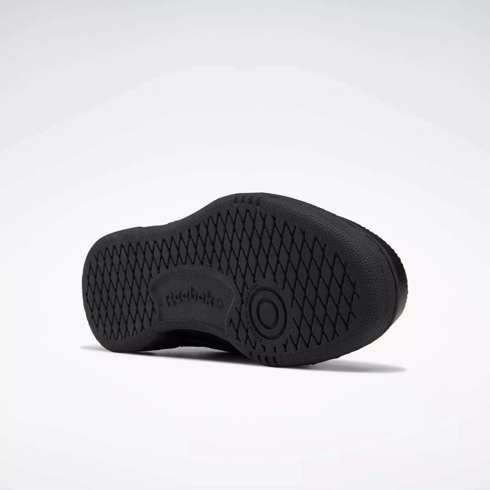 The image shows the sole of a black Reebok Kids' Club C Shoe - Grade School, with a high-abrasion rubber outsole, diamond-patterned grip, Reebok logo, and a circular design at the center. The background is plain white.
