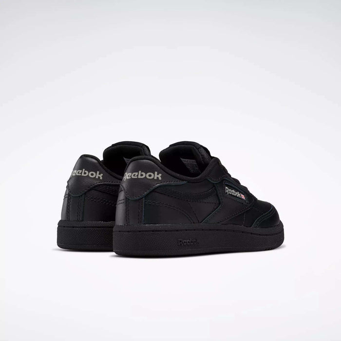 A pair of Kids' Club C Shoes by Reebok, featuring a black leather upper with dark green accents and visible Reebok logos on the heel and side, shown from the back and side on a plain white background.