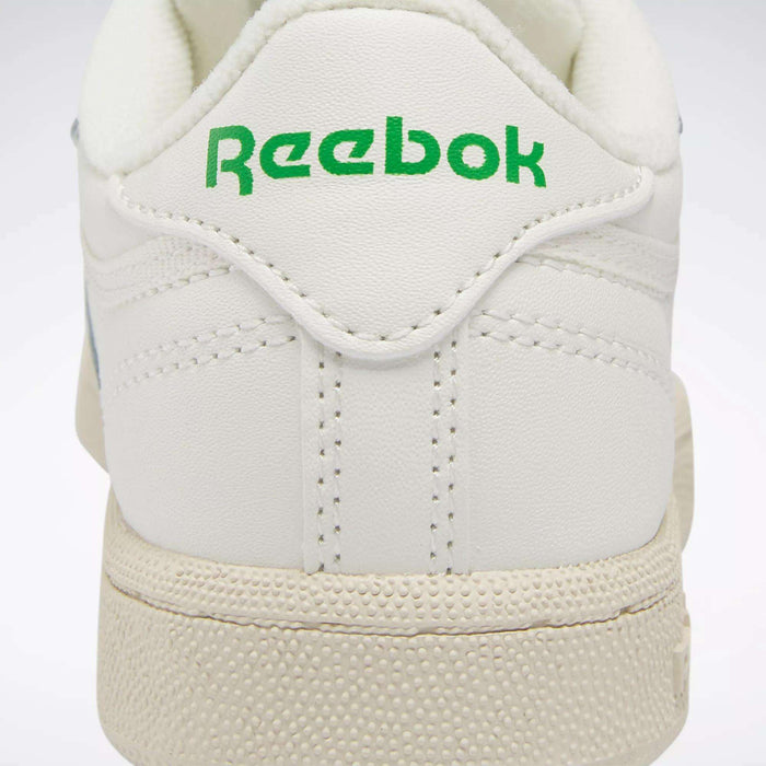 Close-up of the back of a white Reebok Kids' Club C Shoe for preschoolers, featuring "Reebok" in green on the heel tab, textured off-white soles, and detailed stitching inspired by '80s style.