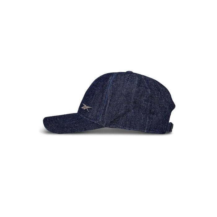 The Reebok Denim Badge Cap is a dark blue denim cap with visible stitching and a small embroidered side logo, featuring a Speedwick sweatband for comfort. Shown in profile against a white background.
