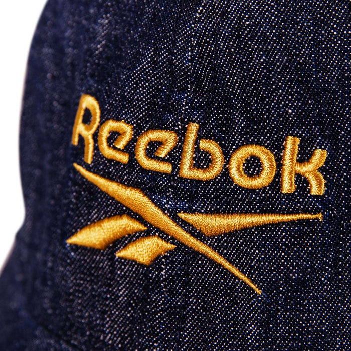 Close-up of the Reebok Denim Logo Cap in blue, featuring a prominent yellow embroidered Reebok logo and text.