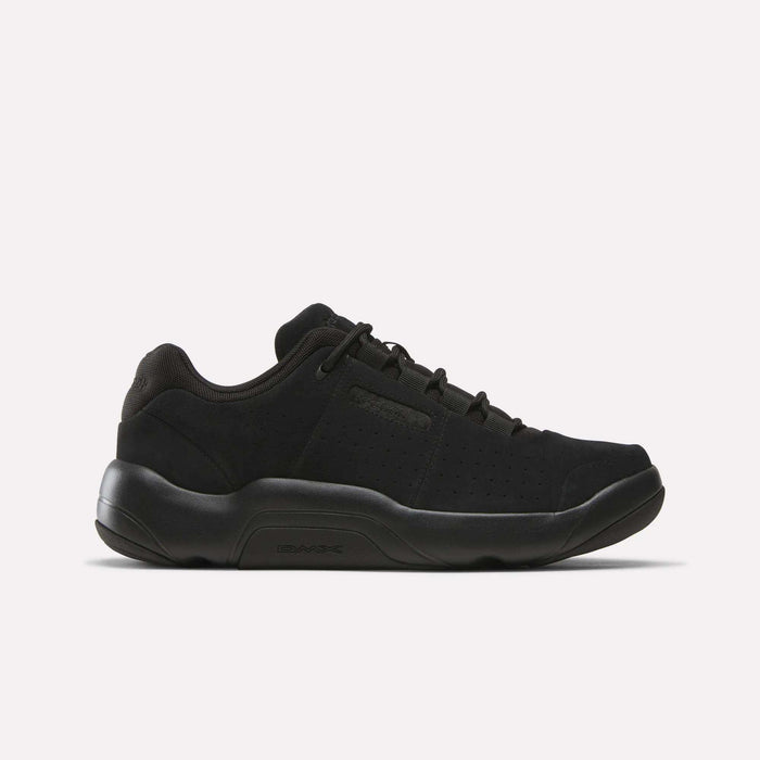 Introducing the Reebok DMX Comfort+ Classic, a black low-top sneaker crafted from premium leather. Featuring a thick sole, lace-up closure, and subtle side perforations for breathability, these shoes are designed with all-day walking comfort in mind. Shown here in Black/Black/Black, displayed in side profile against a plain white background.