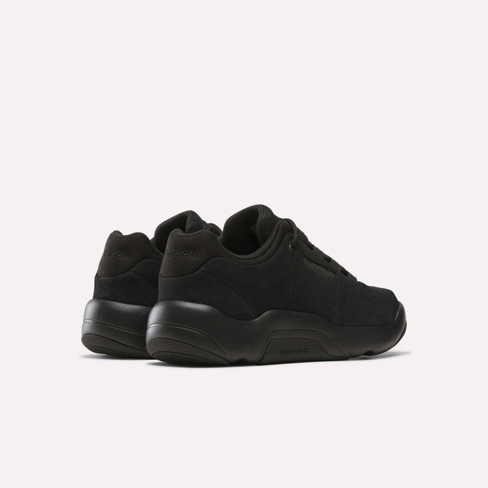 A pair of Reebok DMX Comfort+ Classic black athletic sneakers made from premium leather with thick soles, shown from the back and side against a plain white background.