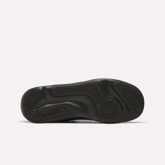 The bottom view of the DMX Comfort+ Classic walking shoe sole from Reebok reveals a black, wavy, textured grip pattern. Designed specifically for walking shoes, this sole incorporates Dynamic air cushioning for superior comfort. An embossed Reebok logo is visible near the heel against a plain white background.