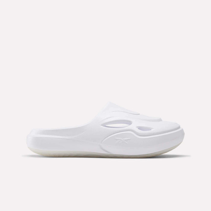 The DMX Recovery Mules by Reebok are white slip-on clogs made of molded EVA with oval cut-out vents and a textured sole. Displayed in a side profile on a plain white background, they evoke the style of classic Reebok mules.