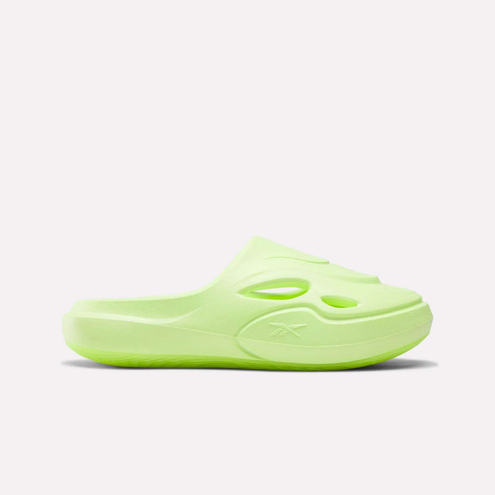 The Reebok DMX Recovery Mules are light green, clog-style slip-on sandals featuring cutout details, a molded EVA upper, and a textured sole. They are shown in profile against a white background.