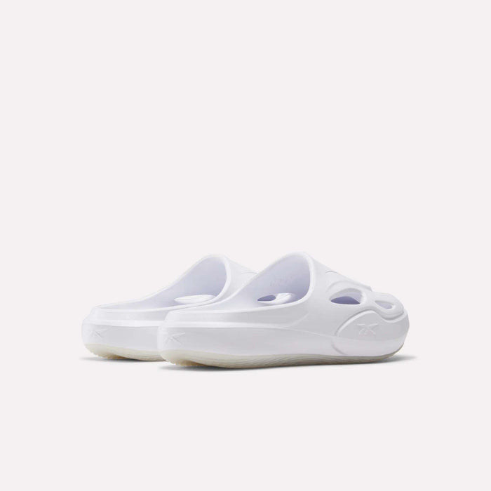 A pair of Reebok DMX Recovery Mules in white, featuring a slip-on design, molded EVA construction, cut-out details, and rounded toes is shown from an angled rear view on a plain white background.