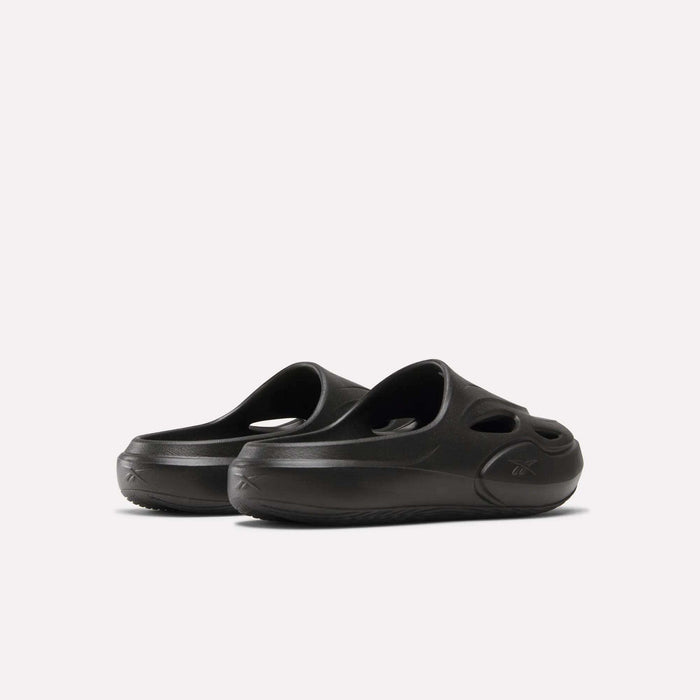 A pair of DMX Recovery Mules by Reebok, black with molded EVA construction, cut-out ventilation holes, and thick soles, displayed on a plain light background.