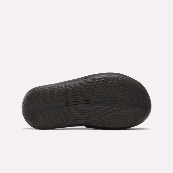 The image shows the black rubber sole of the Reebok DMX Recovery Mules, viewed from below, featuring a textured grip pattern and curved design with molded EVA for added comfort.