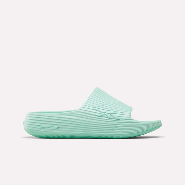 The Reebok DMX Recovery Walking Slides in light teal feature a ribbed texture, open toe, and thick sole with moving air cushioning, displayed in side profile on a white background.