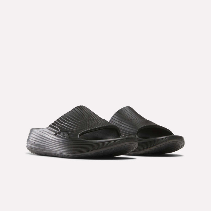 A pair of Reebok DMX Recovery Walking Slides in black, featuring textured ridged surfaces, open toes, and super-soft foam for comfort, shown side by side on a white background.