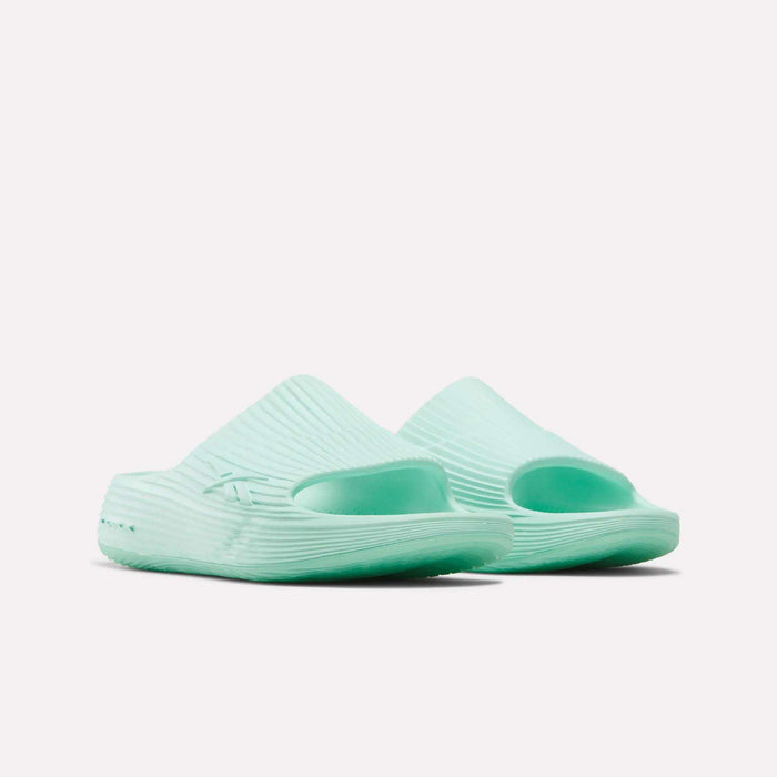 A pair of Reebok DMX Recovery Walking Slides in light mint green with ribbed texture, open toes, thick soles, and moving air cushioning, displayed on a white background.