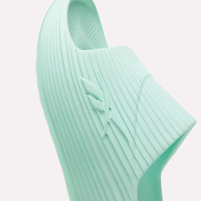 Close-up of a light mint green Reebok DMX Recovery Walking Slide, showing its ribbed texture, raised side logo, and airy foam-like cushioning for comfort.