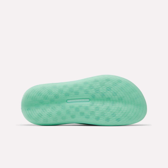 The image displays the light green textured sole of the Reebok DMX Recovery Walking Slides, shown from below on a white background. The wavy tread offers traction and comfort with moving air cushioning technology.