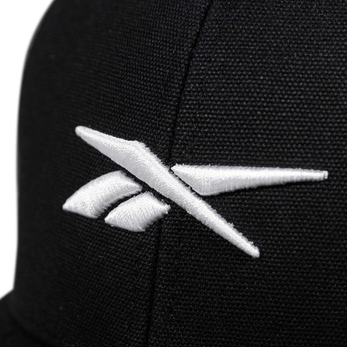 Close-up of the Reebok Embroidered Vector Trucker Cap, a black fabric hat with a white embroidered Reebok logo on the front.