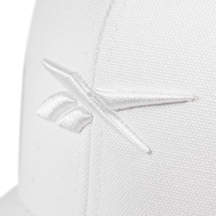 Close-up of the Embroidered Vector Trucker Cap by Reebok, showing a white fabric surface with the Reebok logo stitched in white thread.