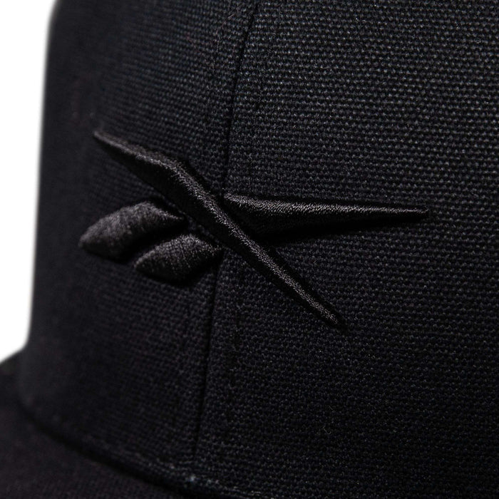 Close-up of the Reebok Embroidered Vector Trucker Cap in black, showcasing the embroidered black Reebok logo on the front with visible stitching and fabric texture.