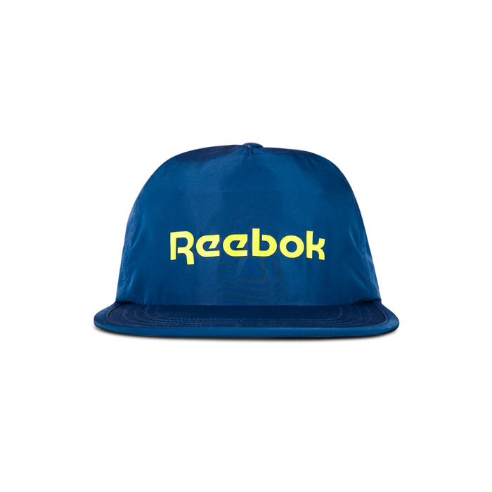 The Reebok Flat Brim Running Cap is a blue, lightweight hat with moisture-wicking fabric, featuring a flat brim and bold yellow Reebok logo on the front, shown against a white background.