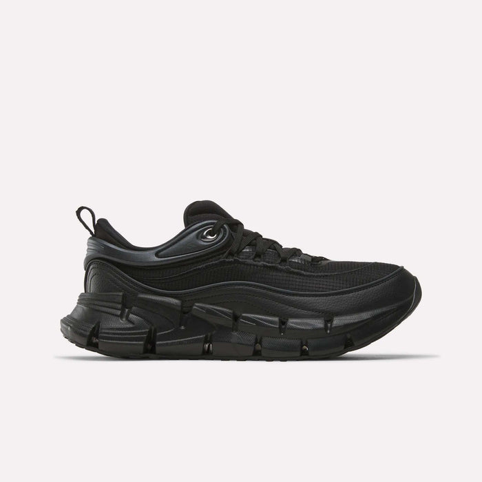 The Reebok Floatzig Encore Running Shoes in Black/Black are athletic sneakers inspired by Reebok’s running heritage, featuring a chunky sole, mesh upper, lace-up front, and a pull tab at the heel. Designed for walking and fitness, they are displayed against a plain white background.