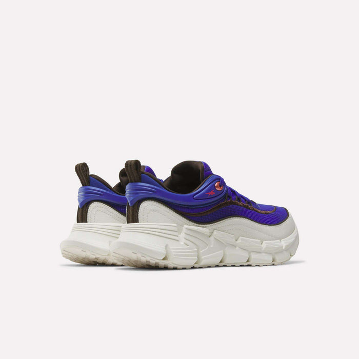 A pair of Reebok Floatzig Encore Running Shoes featuring chunky white thick soles, purple uppers with black and brown accents, and convenient pull tabs at the heel, displayed against a plain light background. Ideal for walking and fitness, these shoes offer bold Zig tech style combined with superior comfort.