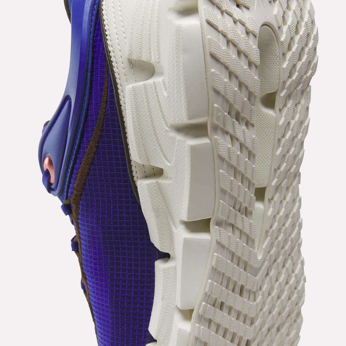 Close-up of the white textured sole of a Reebok Floatzig Encore Running Shoe, featuring a blue and brown upper, shown from a low angle on a white background—a stylish choice for walking and fitness.