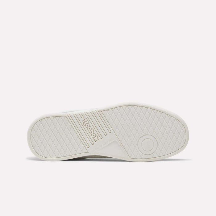 The image displays the white rubber sole of the Reebok Forte Pitch Shoes - Big Kids sneaker, shown from the bottom with a textured grip pattern, grooves, a circular mark, and the Reebok logo embossed in the center—emphasizing its court-inspired design.