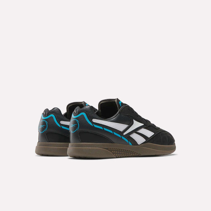 A pair of Reebok Hammer Street Shoes is shown against a plain white background, featuring black uppers with white stripes, blue accents, and brown soles. The soccer-inspired shoes are angled to display both the back and side views.