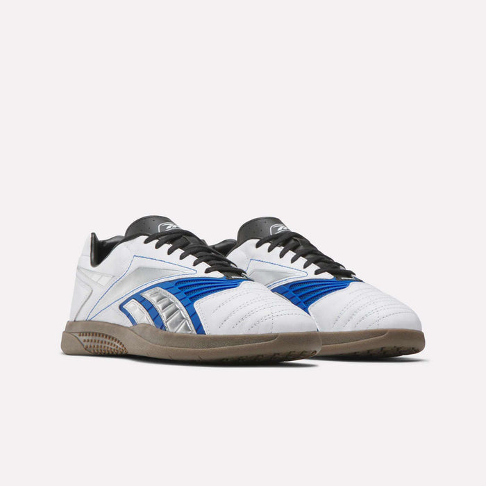 The Reebok Hammer Valde Shoes feature white leather uppers, blue and silver accents, black laces, and brown rubber soles—perfect as indoor soccer boots. Displayed on a plain white background.