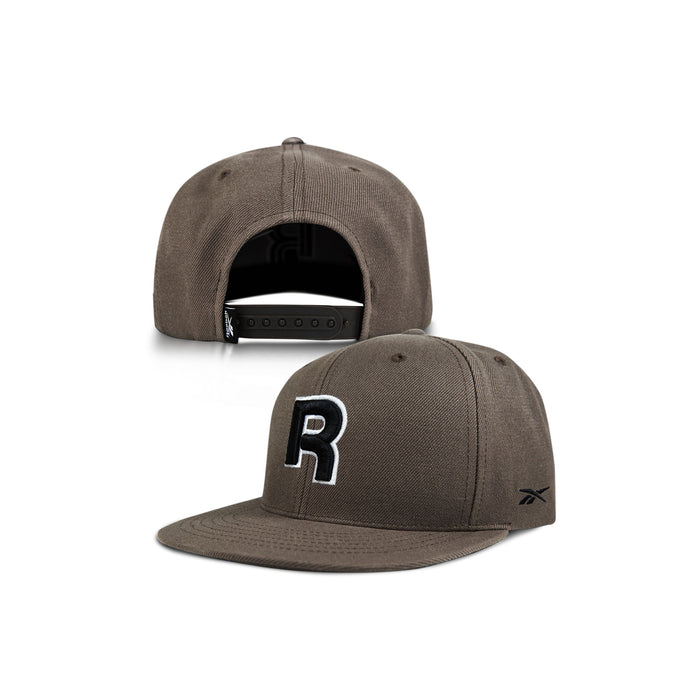 Two views of the Reebok Identity Drop R Cap: one shows the adjustable snapback, flat brim, and bold black-and-white letter R on front; a small Reebok logo appears on the side of the brim.