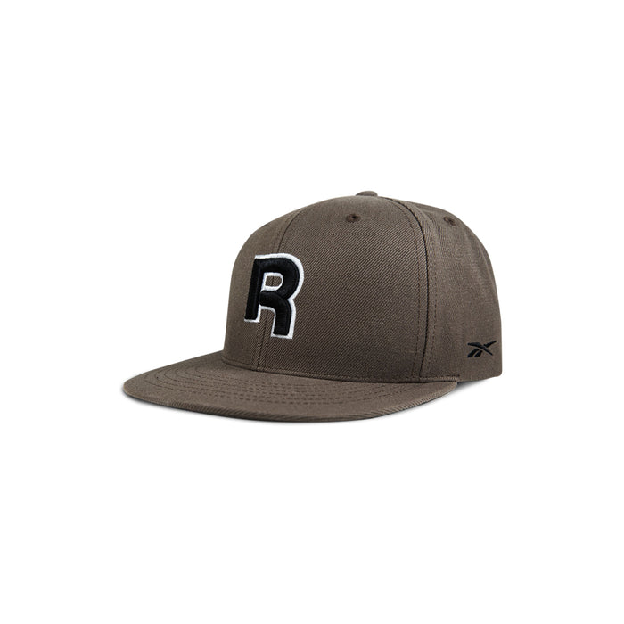 The Reebok Identity Drop R Cap features a flat brim, large black and white R on the front, small side logo, and a snapback closure. Shown in brown on a white background.