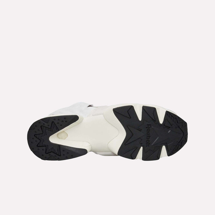 Bottom view of the Reebok Instapump Sliver LTD Shoes in white, highlighting a black rubber outsole with distinct geometric tread patterns and the centrally placed Reebok logo. Equipped with advanced Hexalite cushioning, this model blends superior comfort and performance. The background is plain and light-colored.