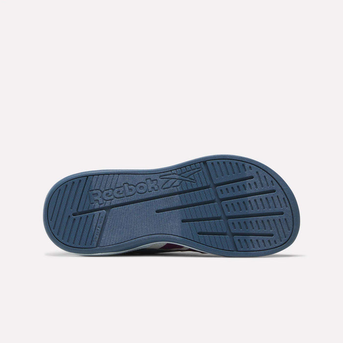 The image displays the blue rubber sole of the Reebok Kids' Nano Play Slip-on, viewed from below. The sole features multiple grooves along with the embossed Reebok logo and its signature vector symbol at the center.