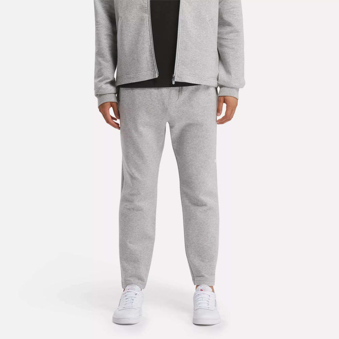 A person in a light gray zip-up jacket and Reebok Men's Active Collective DreamBlend Pants with white sneakers stands against a plain light background; their face is not visible.