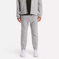 A person in a light gray zip-up jacket and Reebok Men's Active Collective DreamBlend Pants with white sneakers stands against a plain light background; their face is not visible.