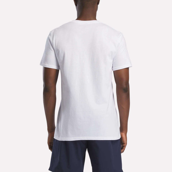 A person stands with their back to the camera, wearing a Reebok Men's Americana Graphic T-Shirt and dark shorts. The background is light and uncluttered.
