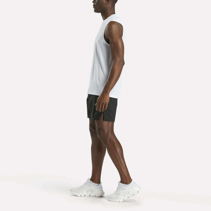 A man in a white sleeveless shirt, black Reebok Men's Athlete Speed Shorts, and white athletic shoes stands sideways against a plain white background.