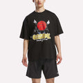 A man in a loose black Reebok Men's Basketball T-Shirt featuring a bold graphic and matching black shorts stands against a plain white background.