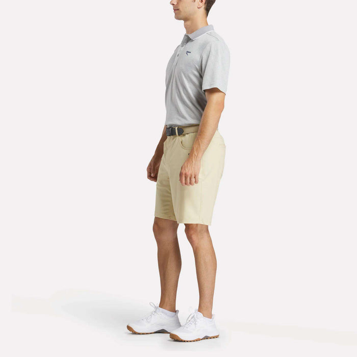 A man in profile wears a light gray Reebok Men's BDC Signature Polo Shirt, beige shorts, white sneakers, and a black belt against a plain white background.