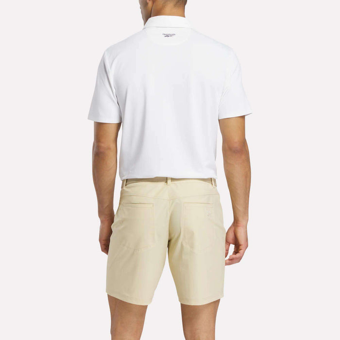 A man faces away from the camera, wearing a white Reebok Men's Bonded Pique Polo Shirt and light beige shorts against a plain background.