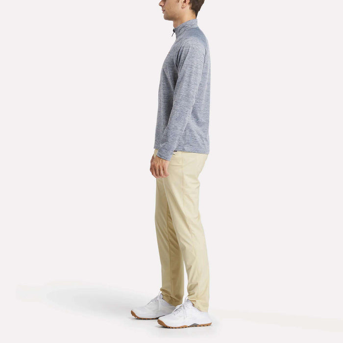 A man stands in profile wearing a light gray Reebok Men's Cationic Wicking Quarter-Zip Sweatshirt, beige pants, and white sneakers against a plain white background.