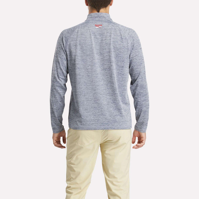 A man stands facing away from the camera, wearing a light grey Reebok Men's Cationic Wicking Quarter-Zip Sweatshirt and beige pants against a plain white background.