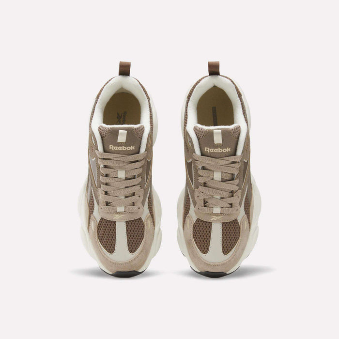 Top view of a pair of beige and brown Reebok Men’s Charge Shoes with white soles and mesh detailing, placed side by side on a plain light background—perfect athletic footwear for men featuring a heritage-inspired design.