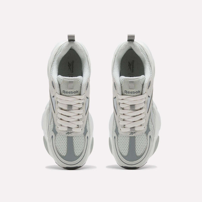 A pair of Reebok Men’s Charge Shoes in white and gray is displayed from above, highlighting the laces, mesh design, and chunky sole. The cushioned midsole provides comfort during workouts, while the Reebok logo appears on the tongue of each shoe.