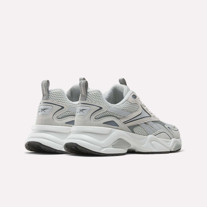A pair of Reebok Men’s Charge Shoes in gray and white, designed with chunky soles, mesh panels, and cushioned midsoles for enhanced comfort. Featuring Reebok logos on the side and heel, these training shoes are displayed on a white background.