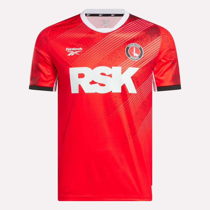 The Men’s Charlton Home Jersey by Reebok features a red design with diagonal patterns, black sleeve cuffs, a white collar, prominent "RSK" sponsor logo, Reebok branding, and a standout club badge on the chest.