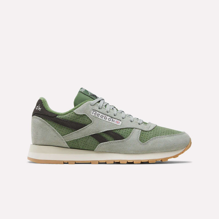 A pair of Reebok Men’s Classic Leather Shoes in Hazygreen, Legacygreen, and Gum is displayed from the side on a plain white background. These sneakers feature a timeless design inspired by the iconic Classic Leather silhouette and are equipped with an EVA midsole for enhanced comfort.