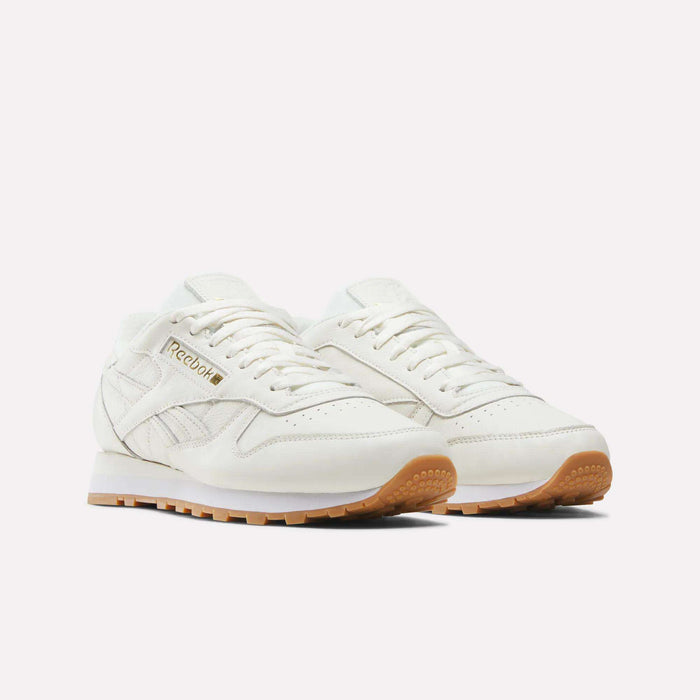 A pair of Reebok Men's Classic Leather Shoes in white, featuring gum rubber soles and a cushioned EVA midsole, displayed on a plain white background.