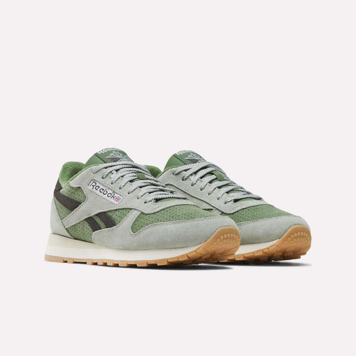 Men’s Classic Leather Shoes by Reebok shown in sage green and grey suede, featuring tan rubber soles and a cushioned EVA midsole, photographed from a slight angle against a plain white background.