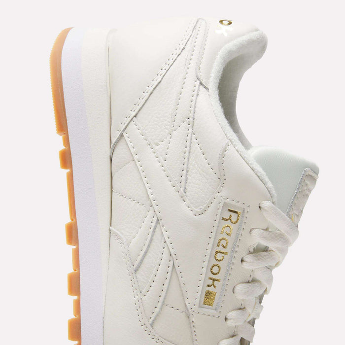 Men's Classic Leather Shoes by Reebok in white, featuring a gold logo, light brown outsole, EVA midsole, and white laces, displayed from a side angle against a plain background.