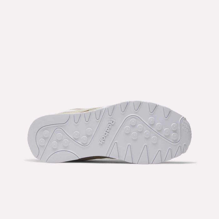 The image displays the white outsole of the Reebok Men’s Classic Nylon Shoes, showcasing an array of patterns such as zigzag lines, circular shapes, and the Reebok logo embossed at the center. Ideal for retro sneaker enthusiasts, these shoes are photographed against a simple, light-colored background.